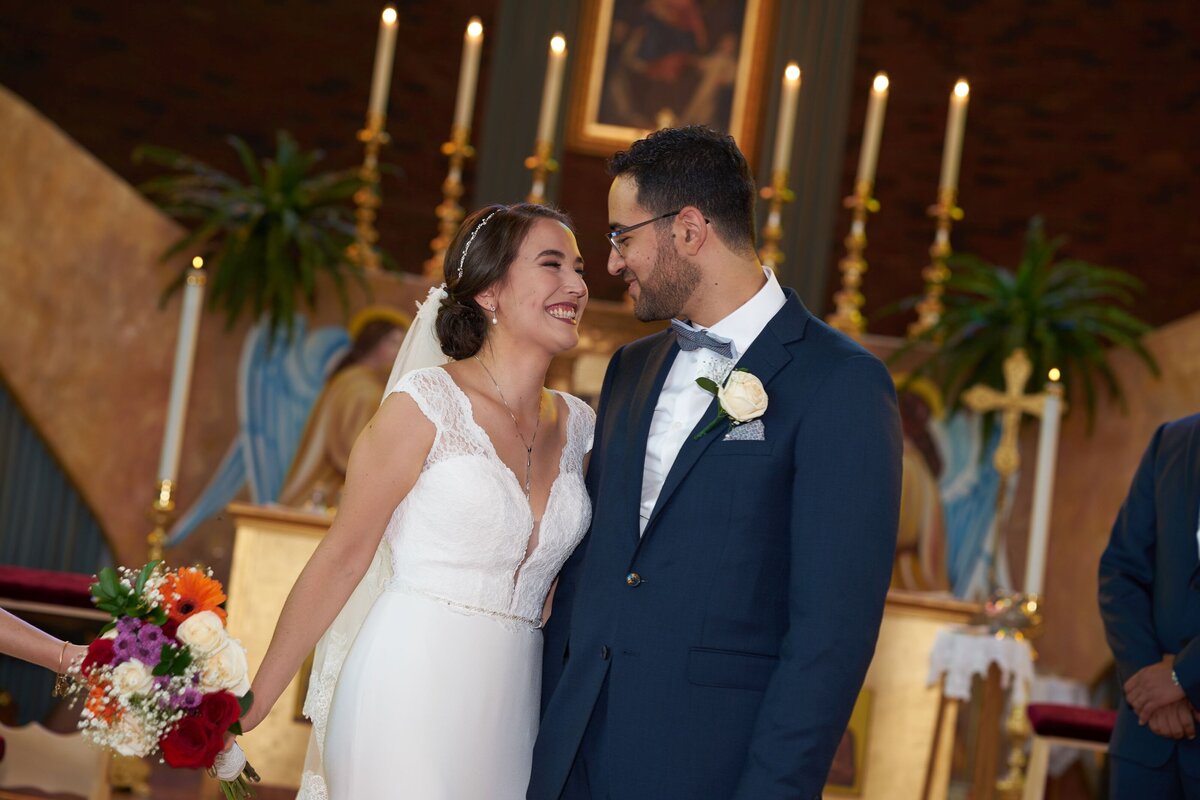 The bride and groom share a loving gaze as they stand together in front of the altar during their wedding ceremony. This intimate moment highlights their connection and commitment, capturing the profound emotions as they exchange vows and begin their journey as a married couple.