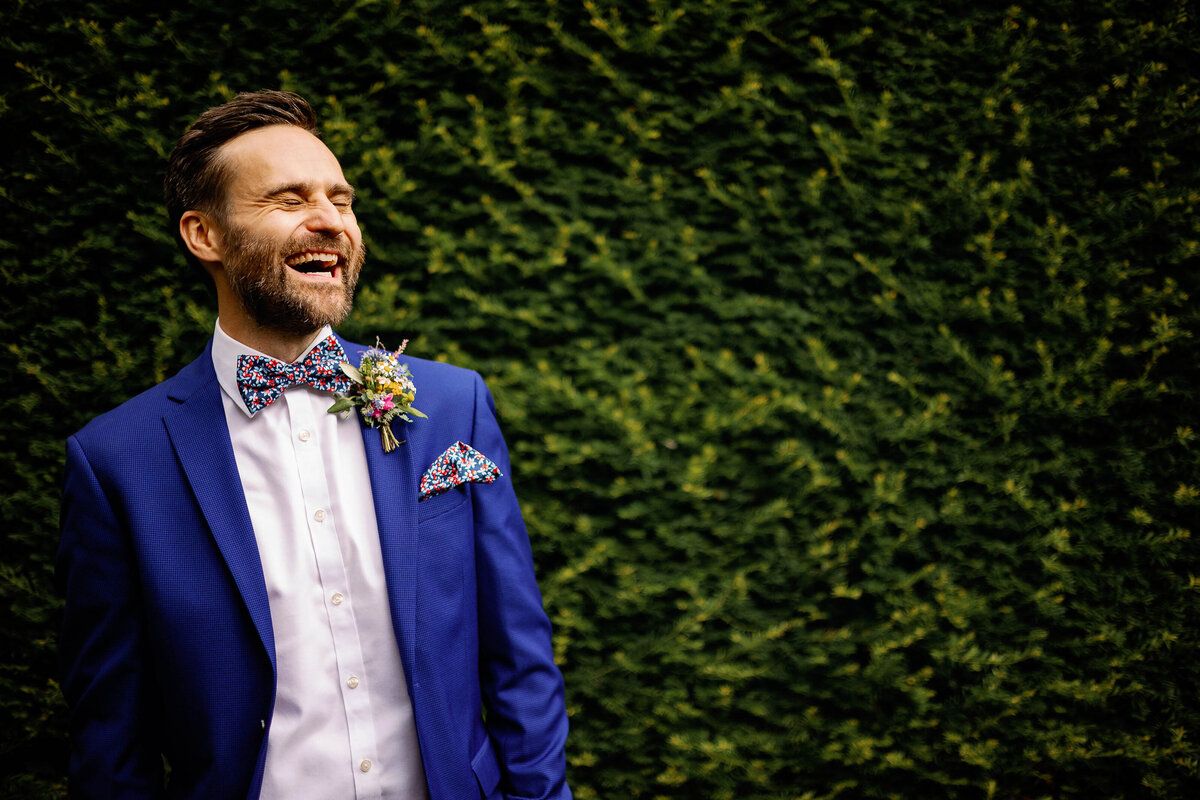 Groom wearing cobalt blue suit and colourful bow tie laughing