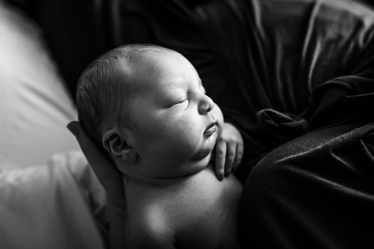 newborn with no shirt sleeping in mom's arms in hospital