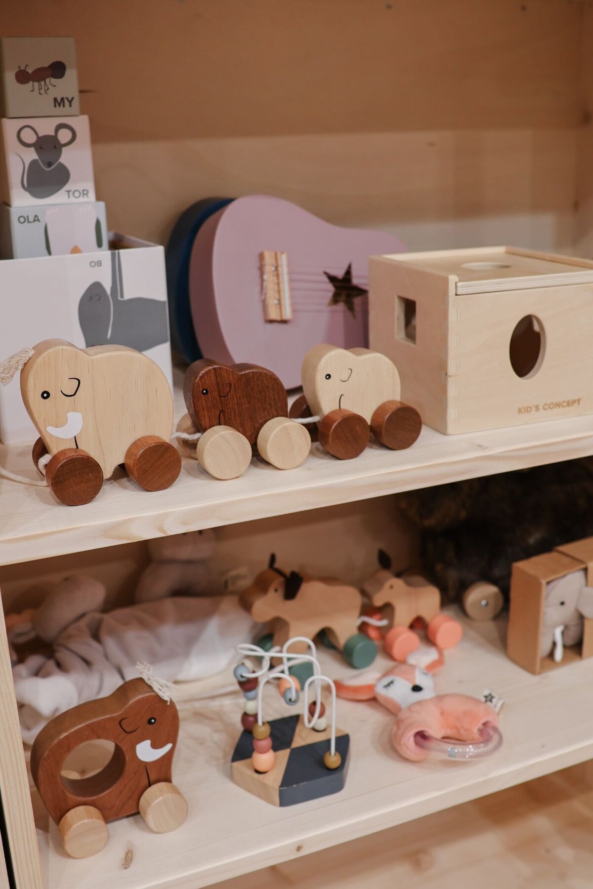 Houten speelgoed uitgestald op planken in een winkel, inclusief olifantjes, een gitaar en een huisje.