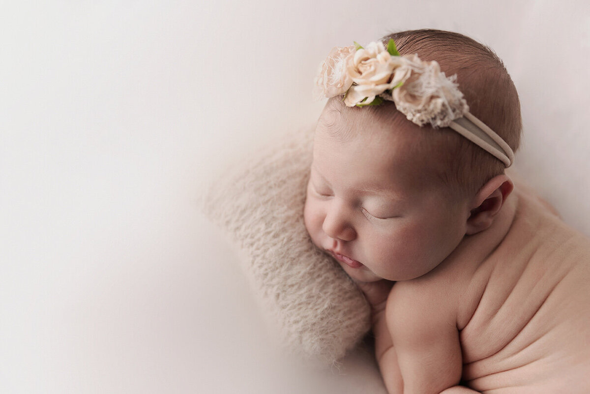 Newborn sleeps on belly with side wrinkles and floral crown.