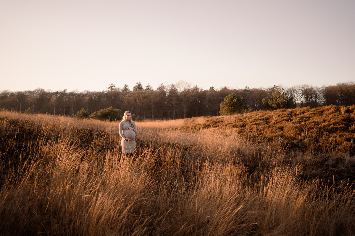 Een wide shot van een zwangere vrouw in de prachtige heide tijdens een zwangerschapsshoot