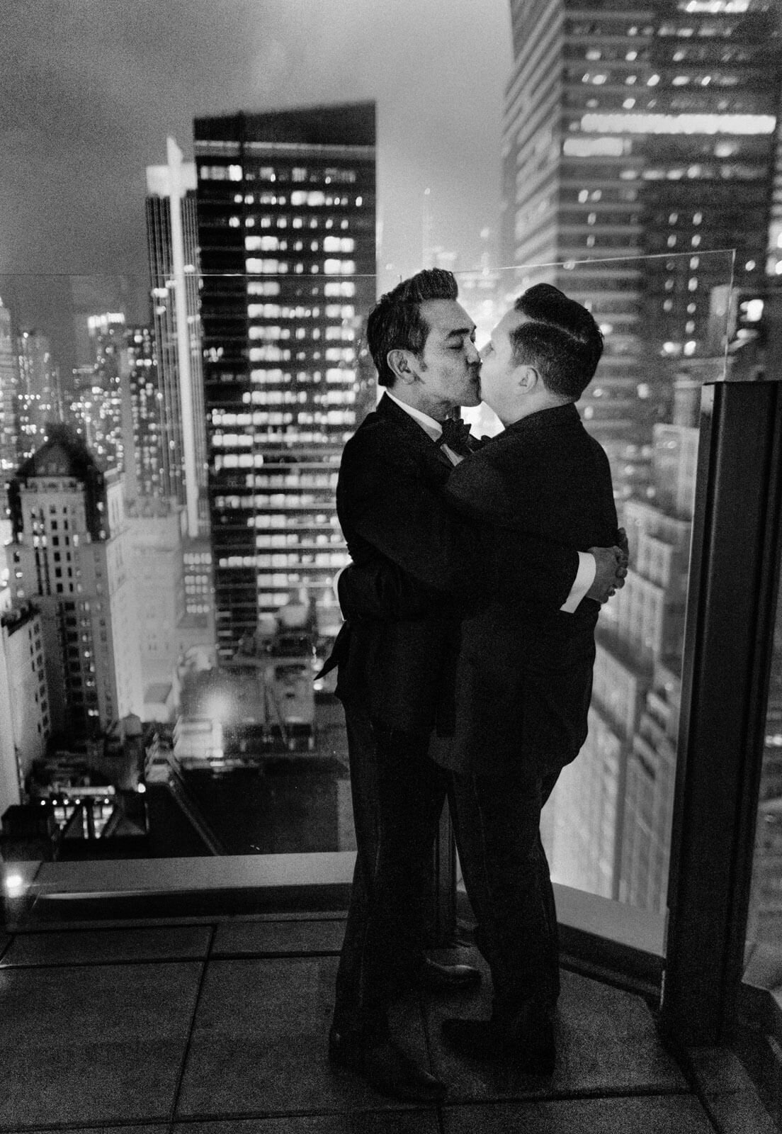 The two grooms are kissing in the veranda overlooking the buildings in The Skylark, New York. Wedding Image by Jenny Fu Studio