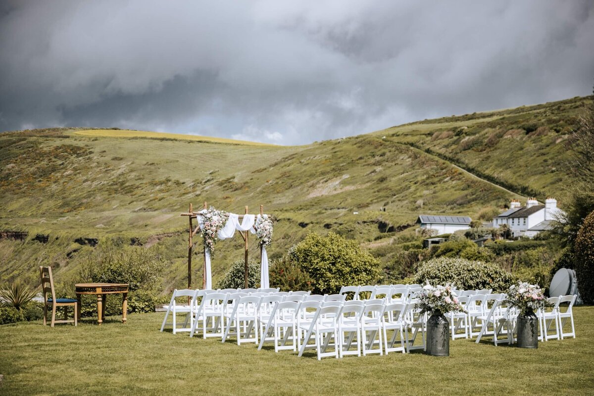 A lawn with rows of chairs and a floral arch at the end of the aisle