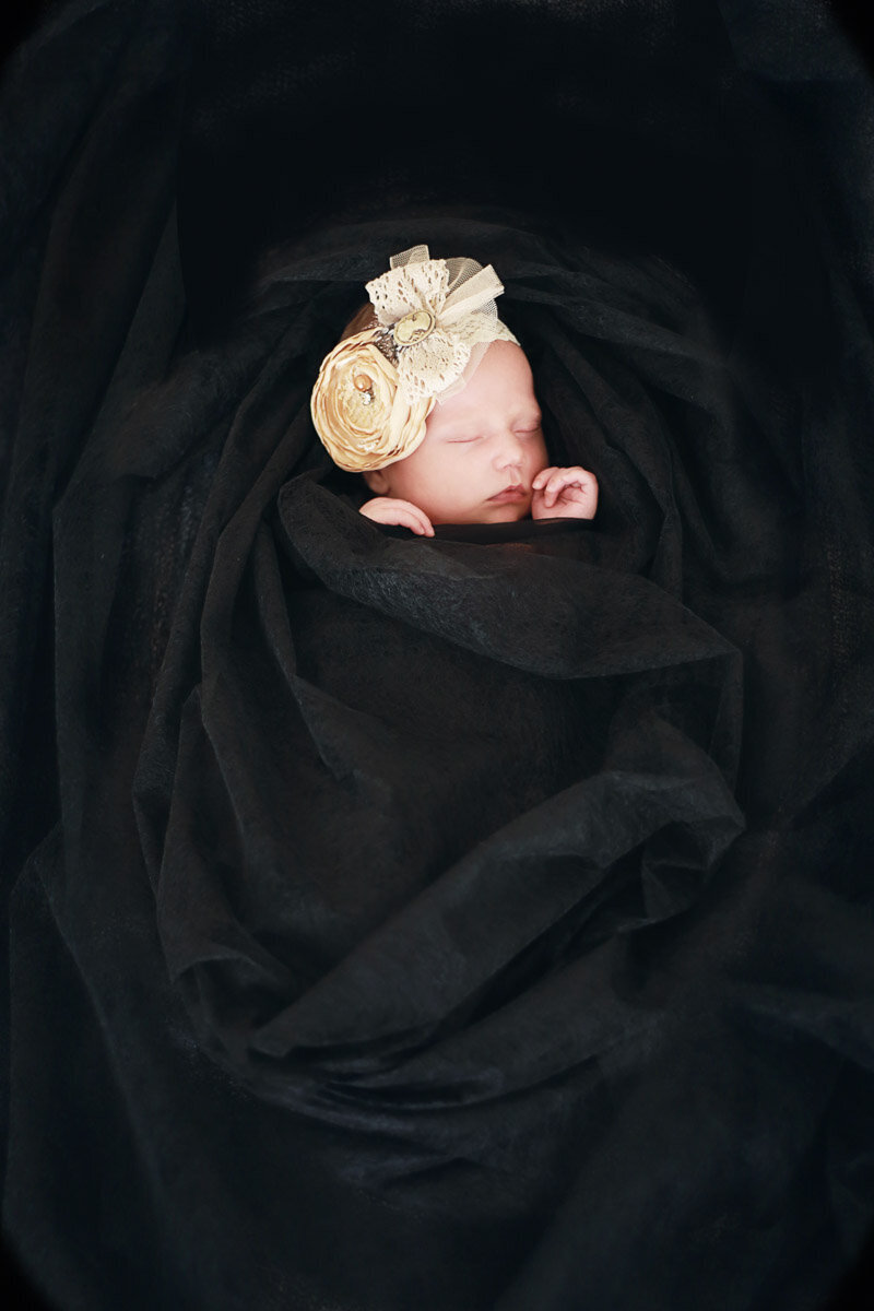 Baby girl wrapped in black silk blanket wearing victorian hairband in home photo session in Calgary Alberta