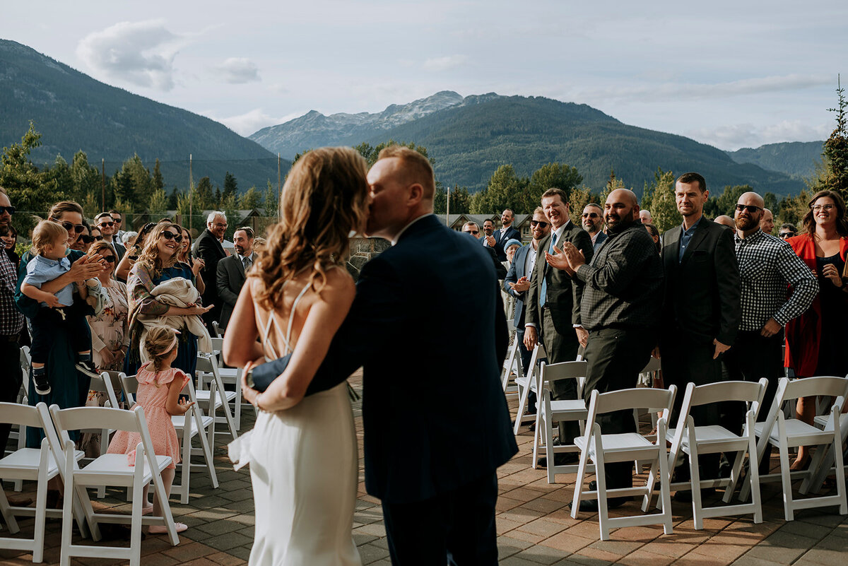 Couple shares kiss after Westin Whistler wedding ceremony with crowd cheering on in the background