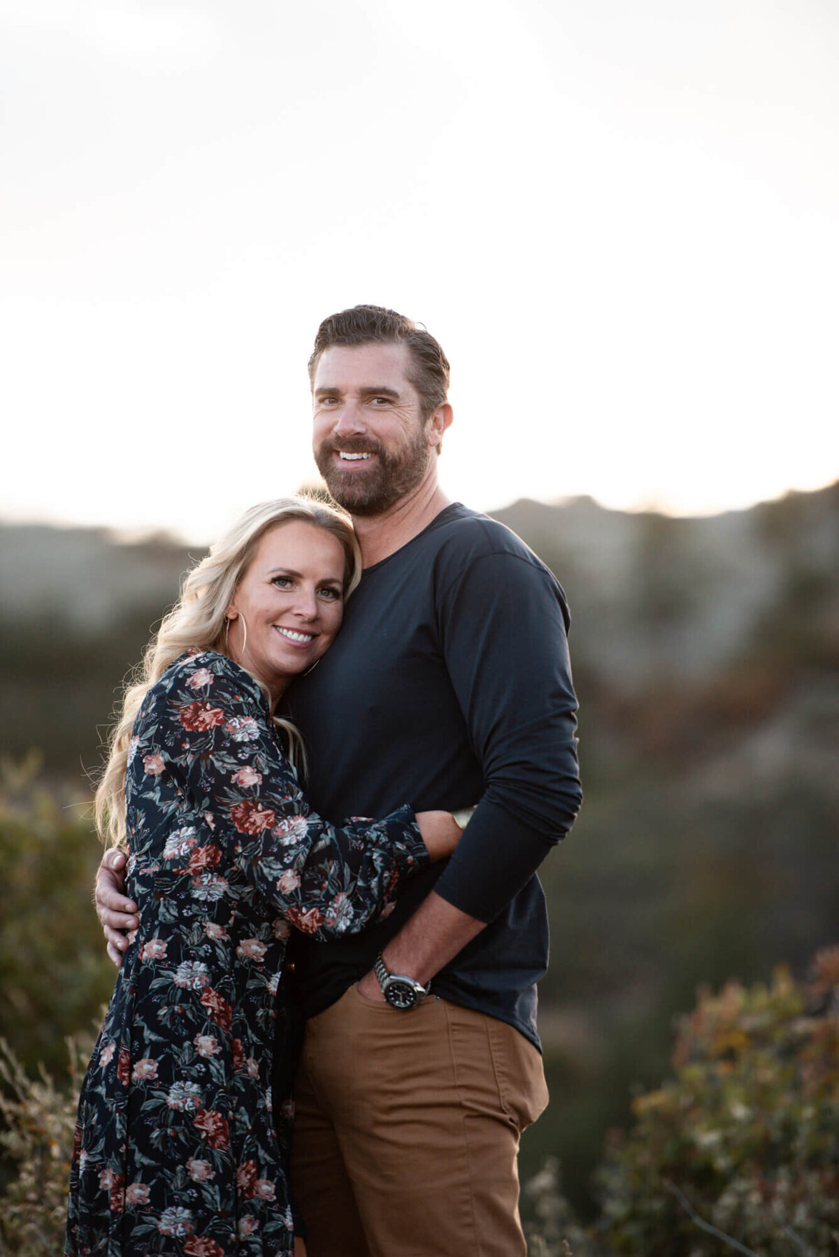 A happy couple in blue hug and smile while standing in the mountains
