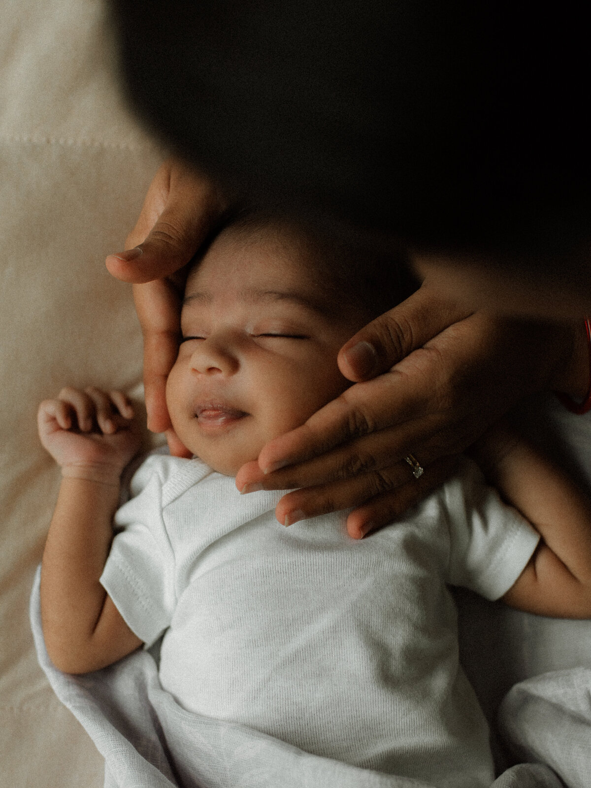 Tender hands cradle a newborn’s smiling face, capturing a quiet moment during a lifestyle newborn photography session.