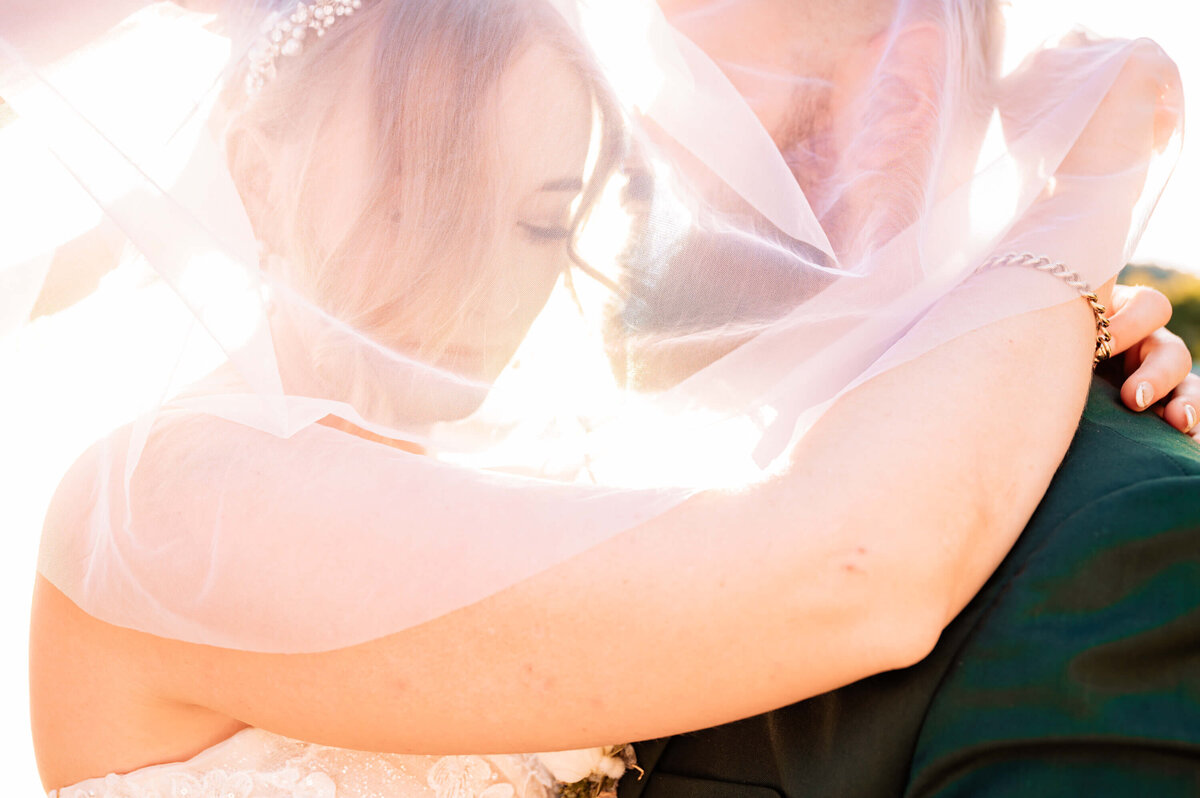 Under a flowing veil, a bride and groom hold each other close, radiating love and joy on their special day. - photo by Jamie Simmons