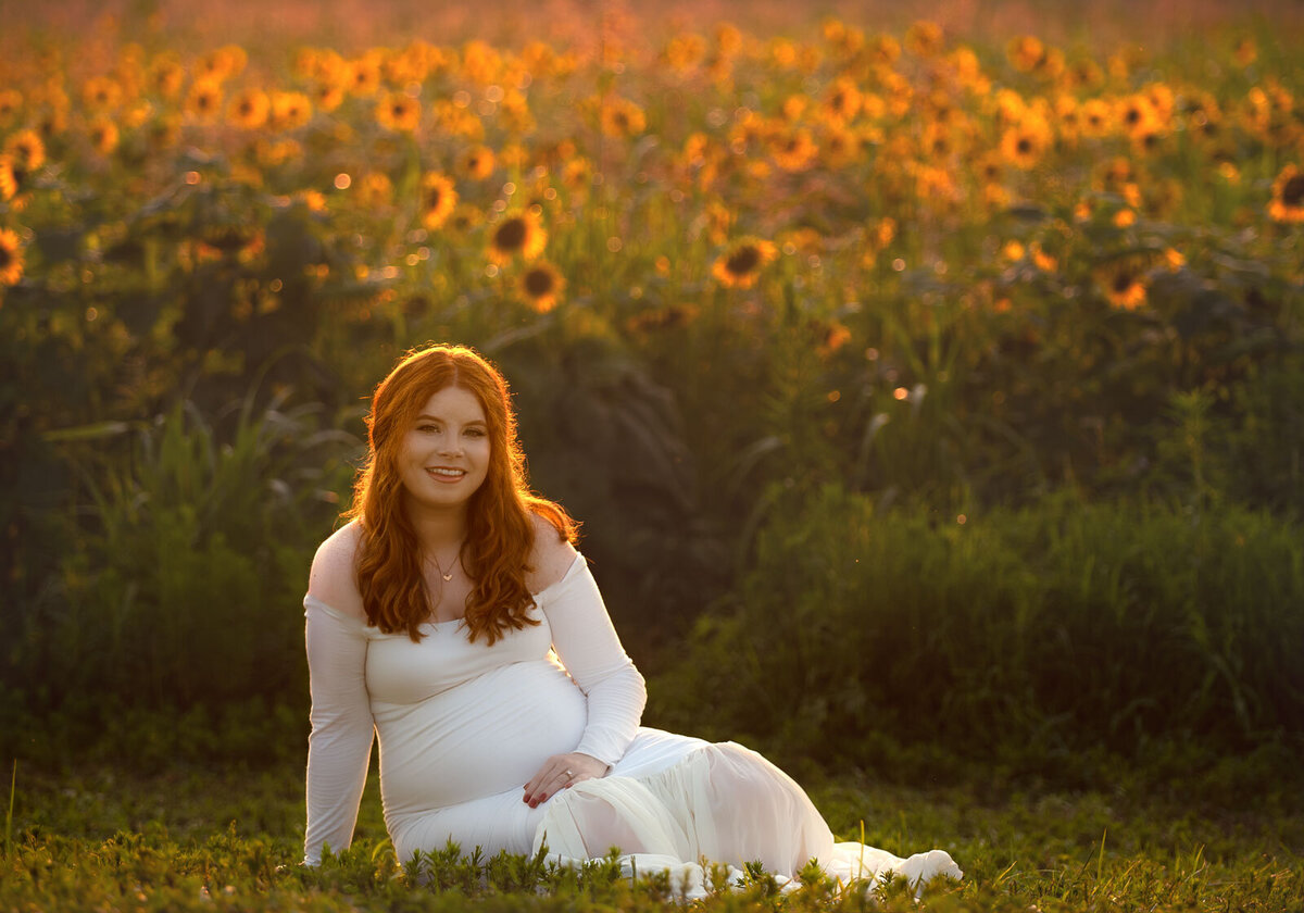 pregnant mom sitting in grass in front of sunflower field by st. louis maternity photographer