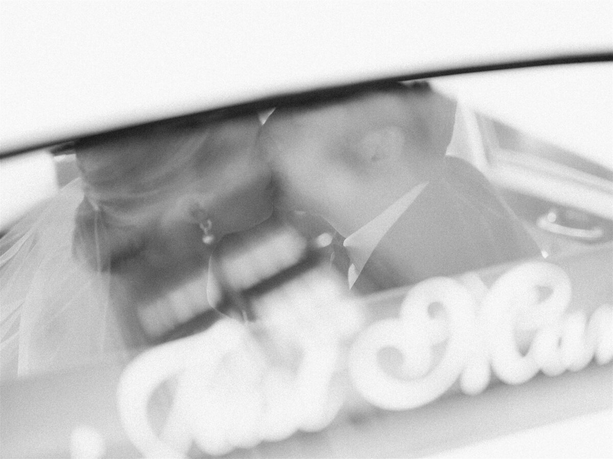 A blurry photo of the bride and groom kissing inside the antique car.