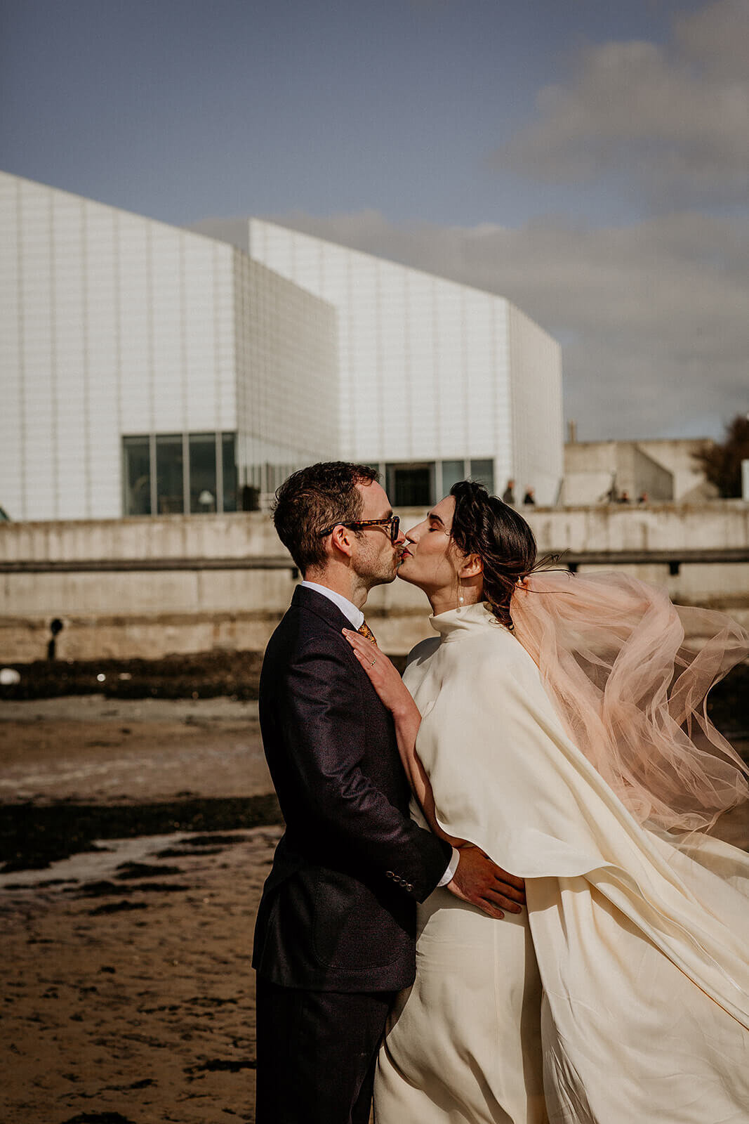 Turner Contemporary wedding couple.  On the beach kissing. Wind blowing peach coloured veil