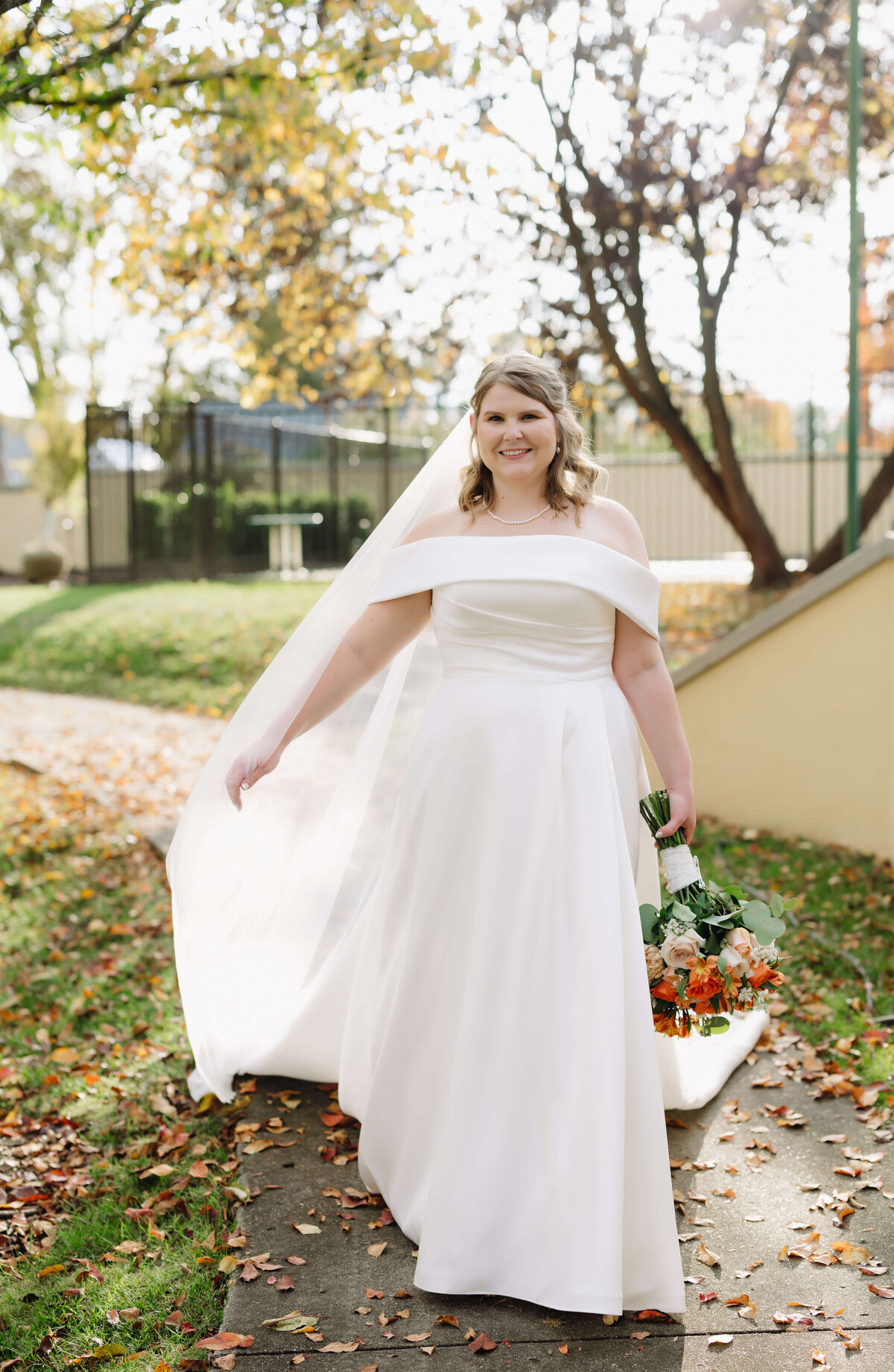 sun set bridal portrait with bride in a soft satin gown with a veil flowing behind her holding her warm toned wedding bouquet to her side for her Richmond weddings