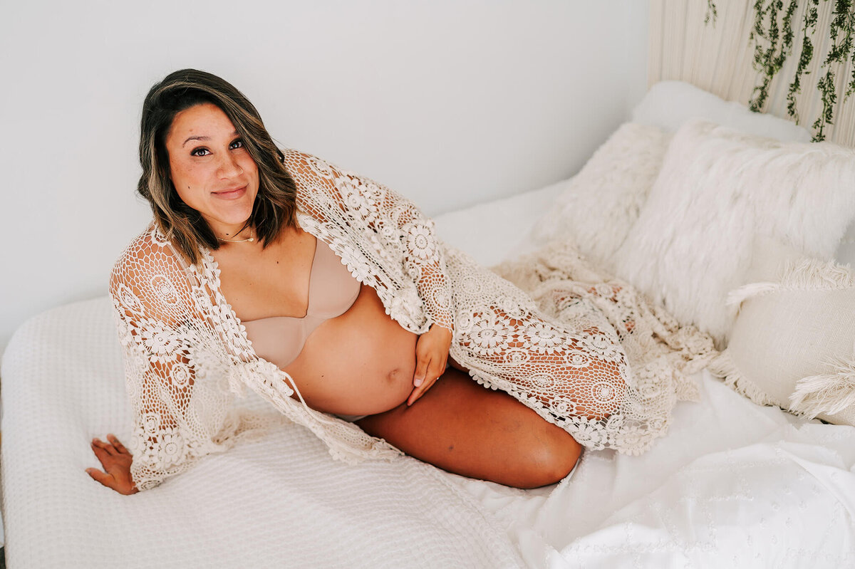 maternity photo of pregnant mom sitting on bed holding baby bump