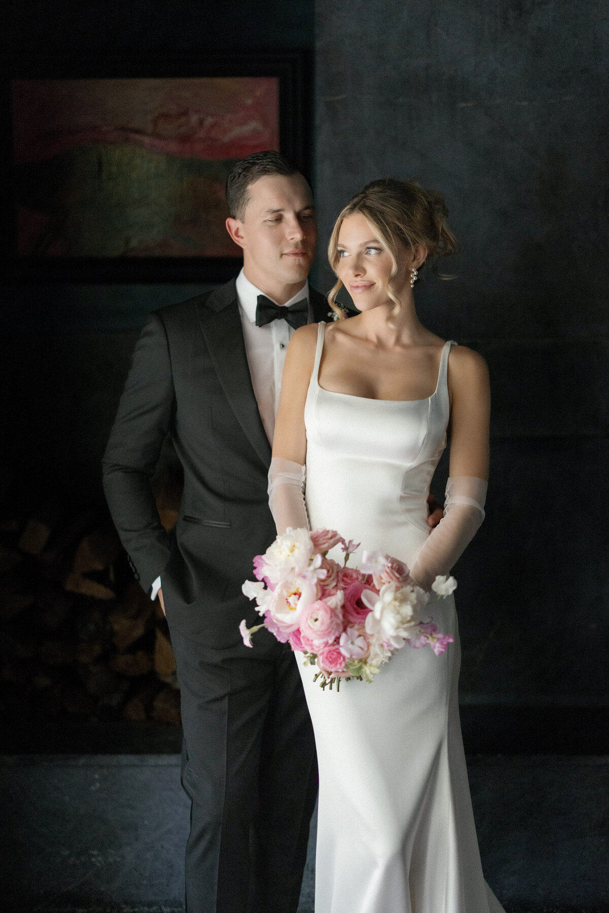groom and bride holding pink bouquet in dark room