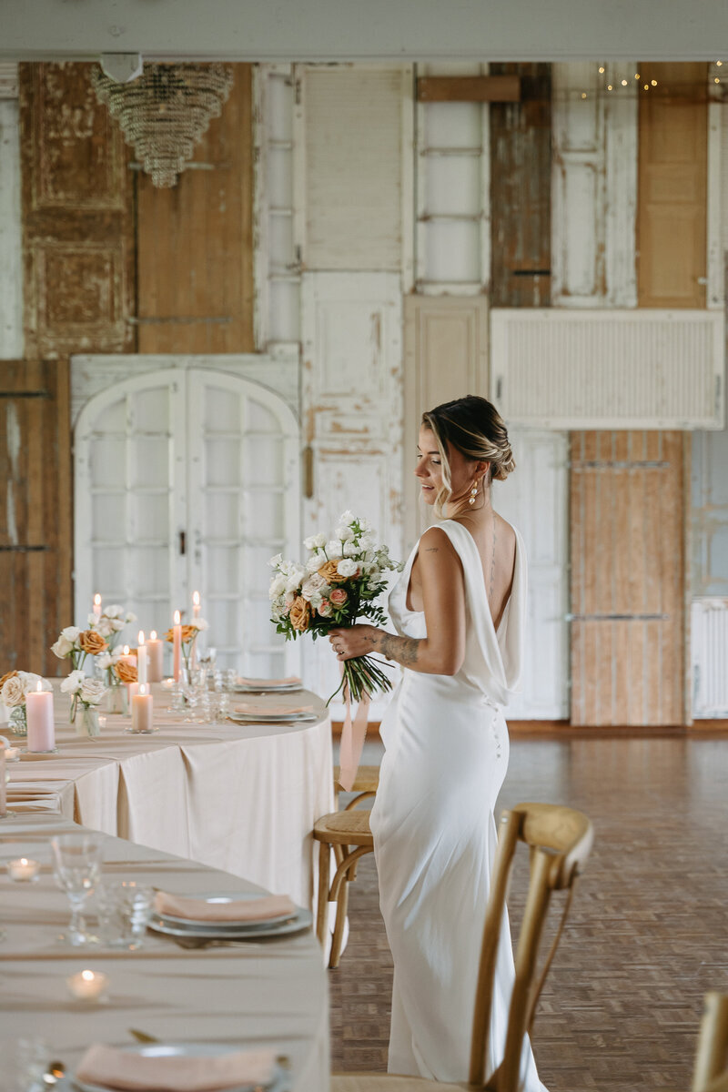Mariée de dos debout face à une table de mariage minimaliste et sinusoidale. Projet organisé par Nos moments Ensemble, wedding planner nantes en Pays de la loire.