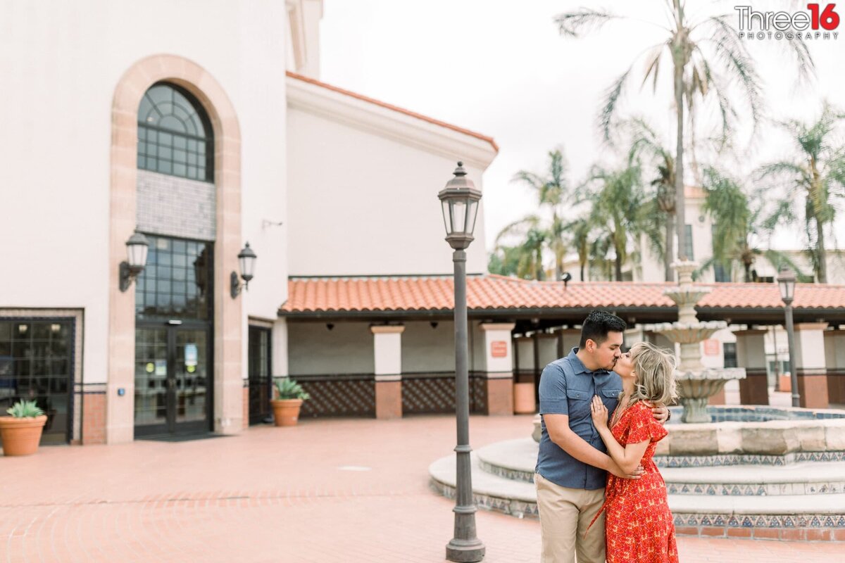 Engaged couple share a kiss in the Santa Ana Train Station courtyard