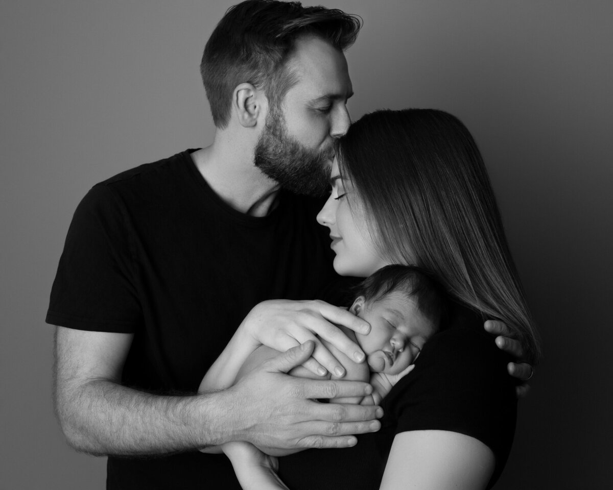 Black and white image of parents holding sleeping newborn with eyes closed in tender moment | Austin newborn photographer serving Round Rock and Liberty Hill