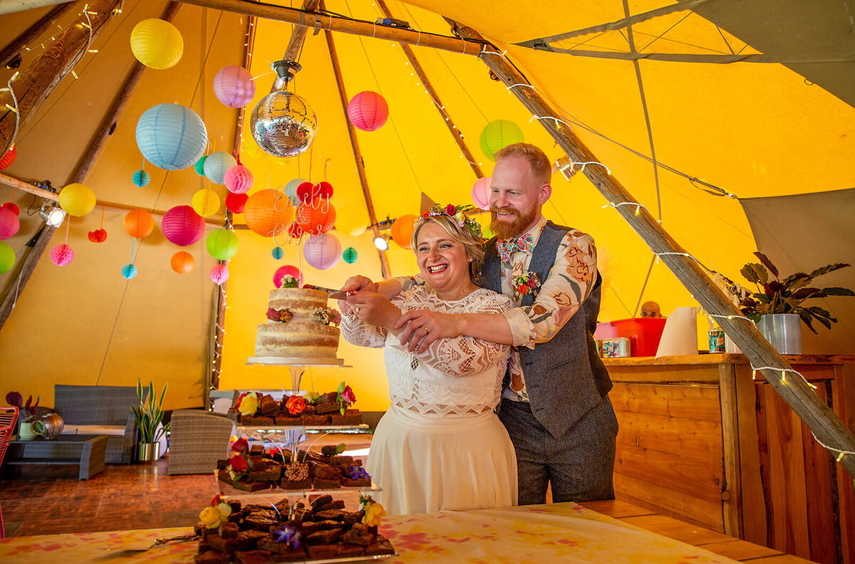 Couple in yurt, cutting wedding cake.