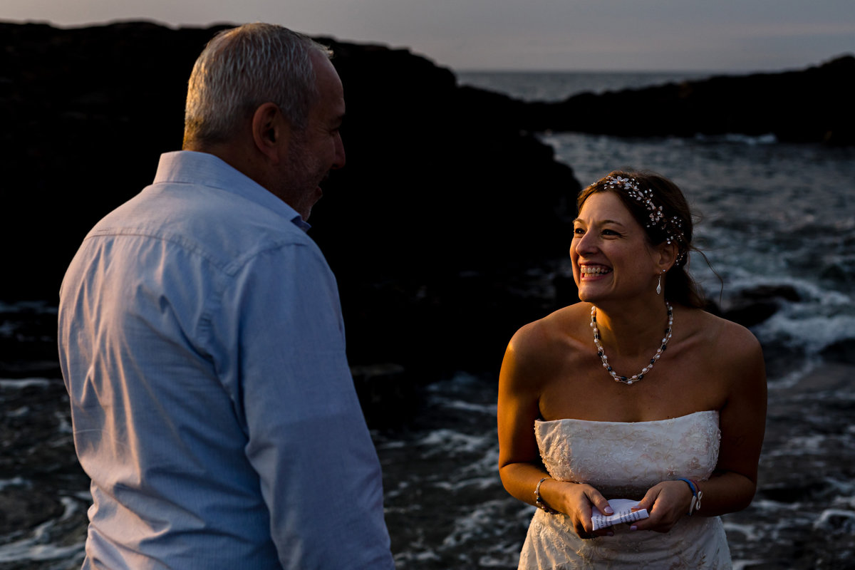 Ogunquit Maine Elopement on the rocks of Marginal Way and the bride laughs after reading her vows at the water's edge
