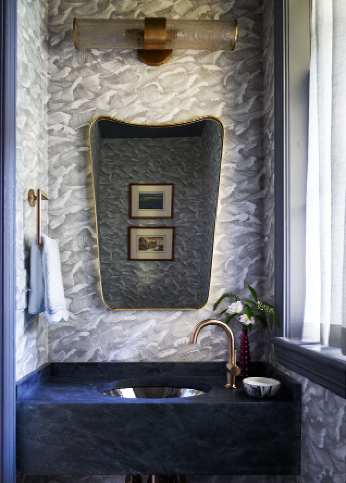 Interior decorators in Hingham create a bathroom with a custom soapstone sink, light grey Cole & Son wave-patterned wallpaper, brass fixtures, and Kelly Wearstler lighting.