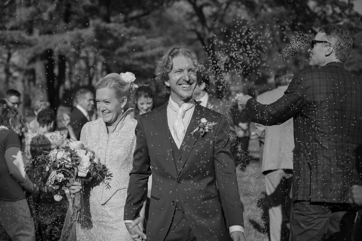 Bride and Groom smile as they walk down the aisle and guests throw rice.