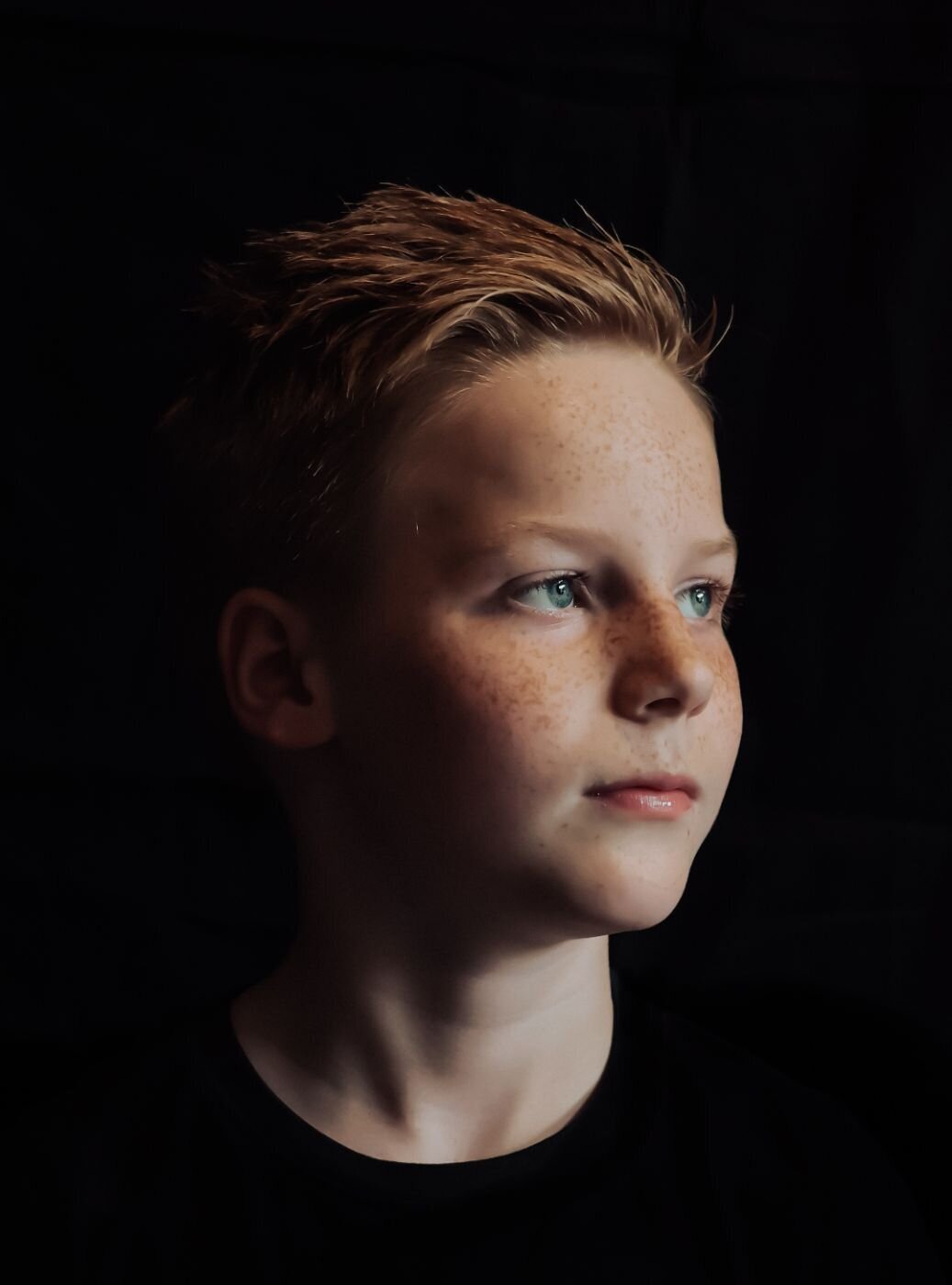 Een portretfoto van een jonge man met een open en vriendelijke uitstraling, gefotografeerd tegen een donkere achtergrond