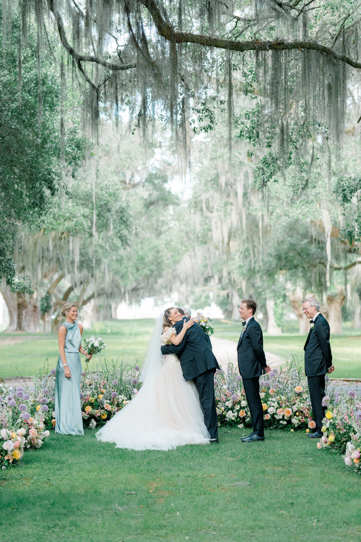 Spring wedding ceremony at Spring Island. Bride hugs her dad. Spanish moss hanging.