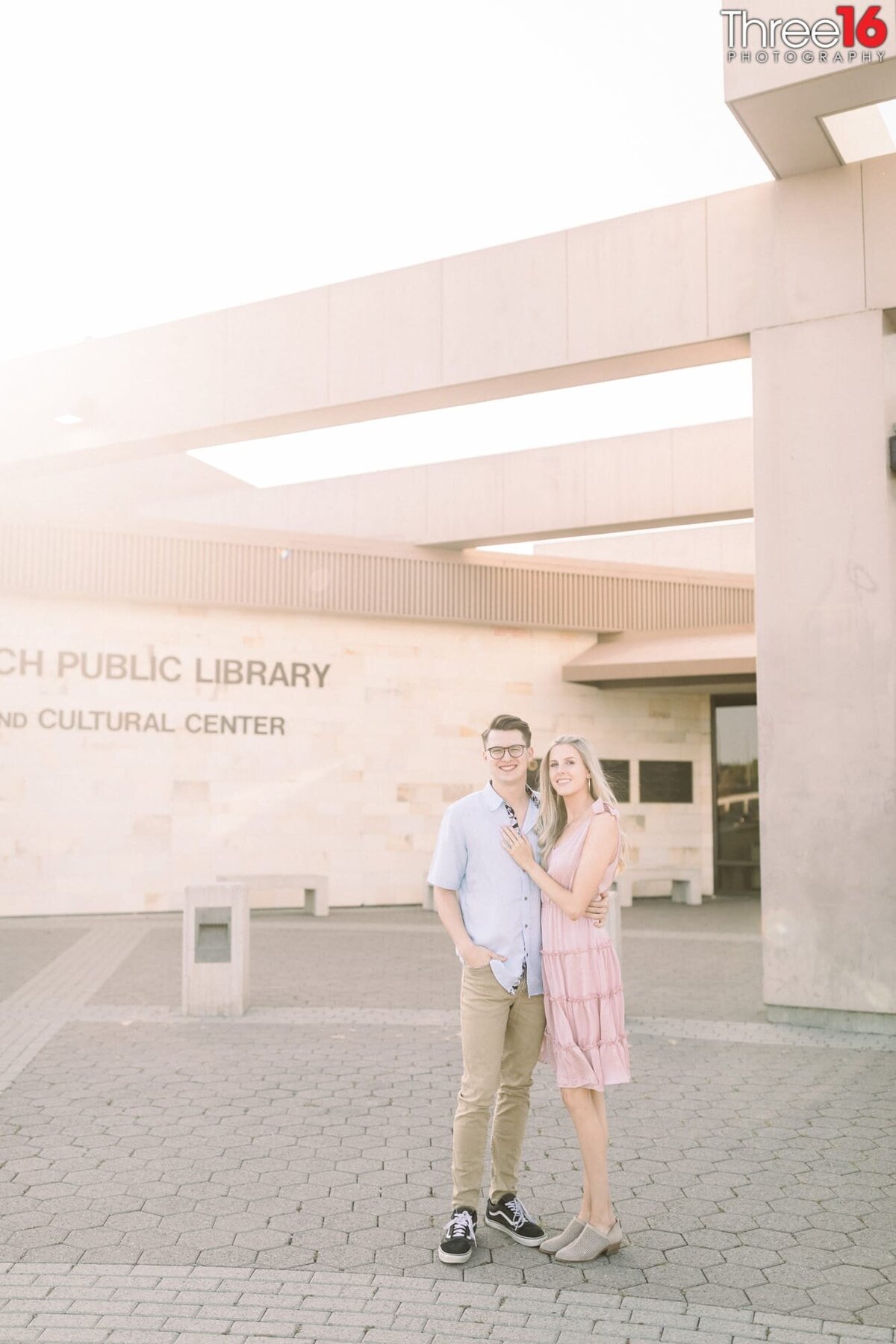 Engaged couple pose together in front of the Huntington Beach Library