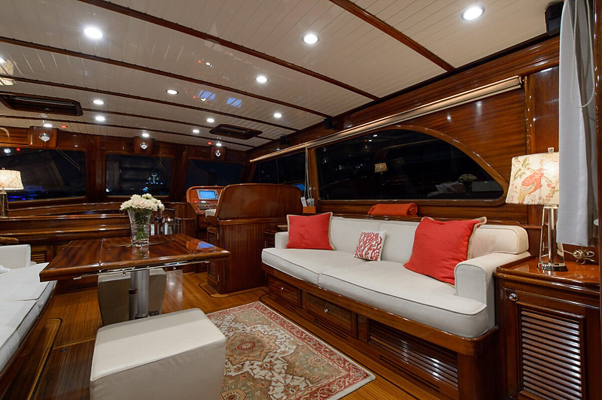 The interior of a luxurious yacht features a cozy seating area with polished wood paneling, plush white sofas adorned with red cushions, and elegant lighting