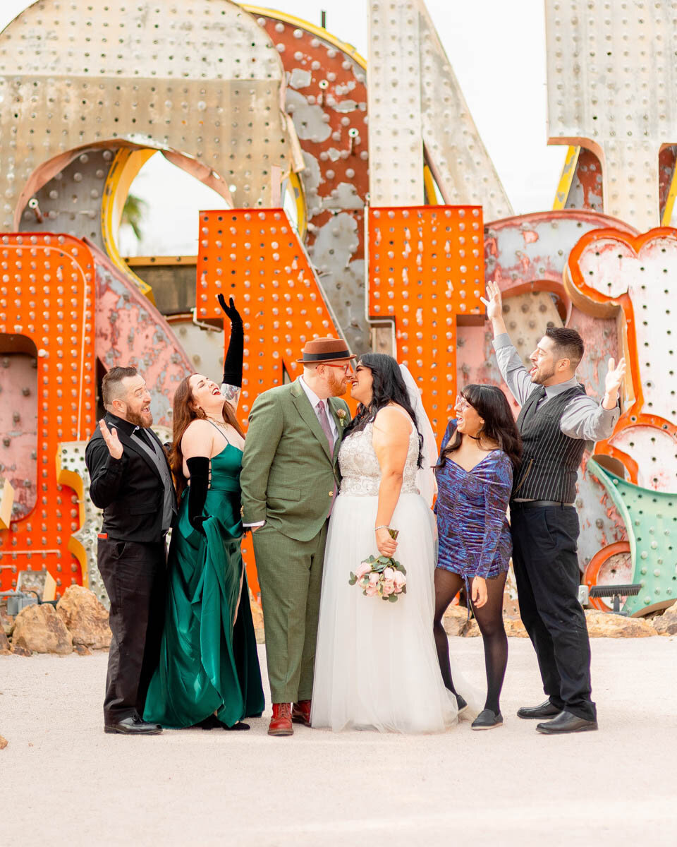 Wedding party cheers as a newlywed couple kiss at the Neon Museum in Las Vegas, NV.