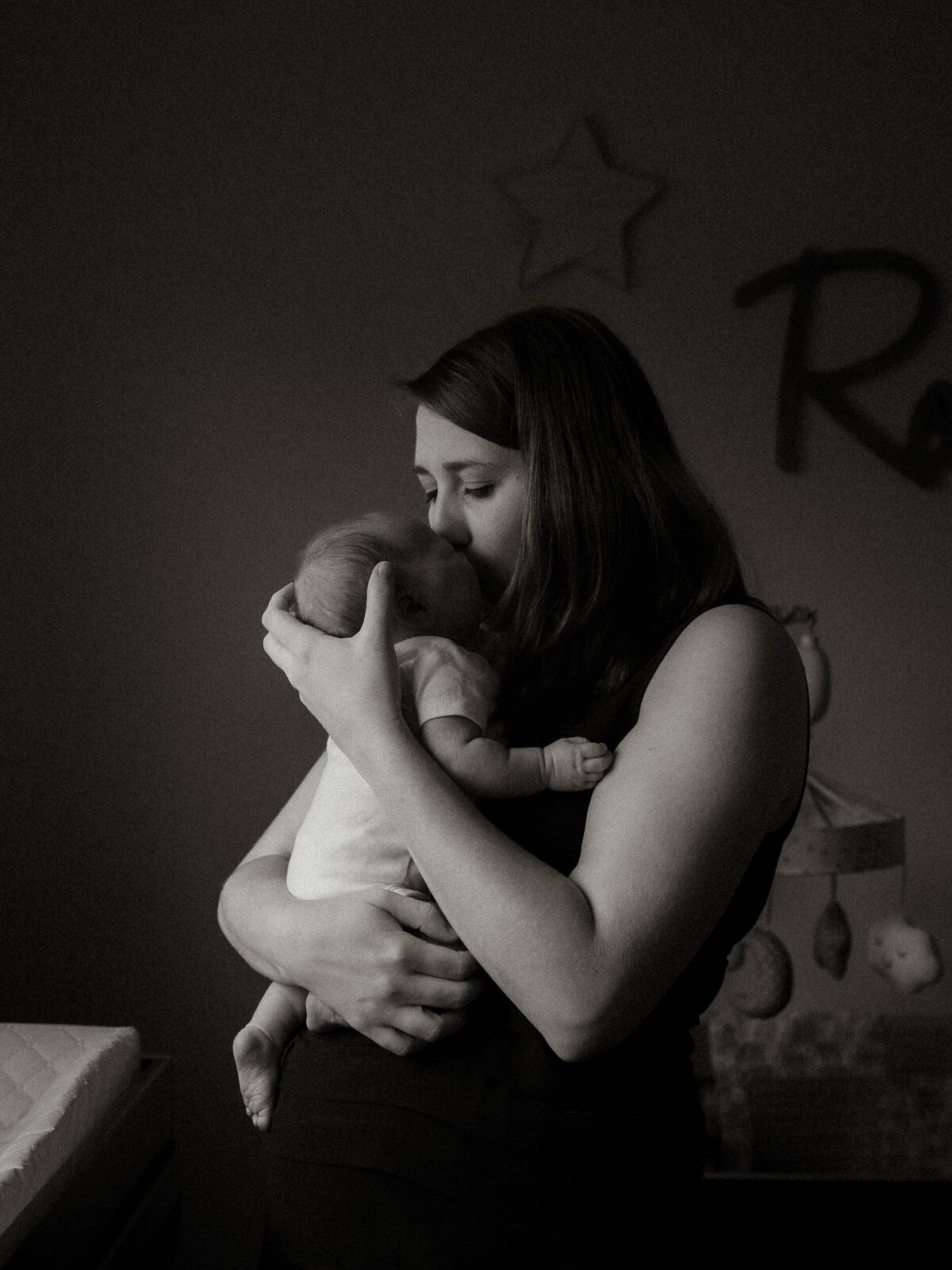 Black and white photo of mother holding newborn in nursery, tender and intimate lifestyle session.