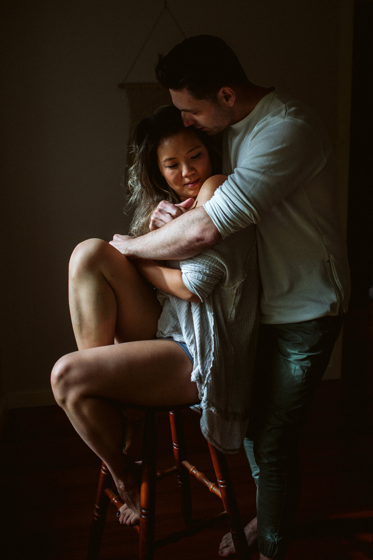In Home Lifestyle Couples Photo Hugging on Chair in natural light. Fun in home couples lifestyle photo. Sapphire and Stone Photography