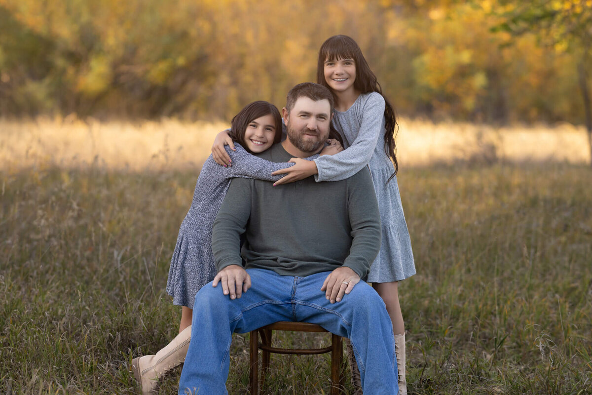 two  young daughters hugging their dad in a field