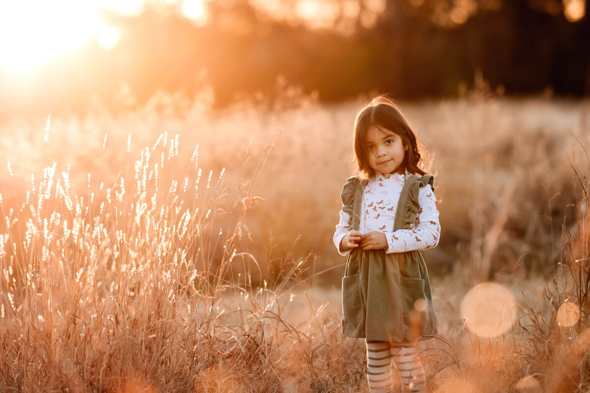 A child in a field wearing a green dress with a golden sunset in OKC.
