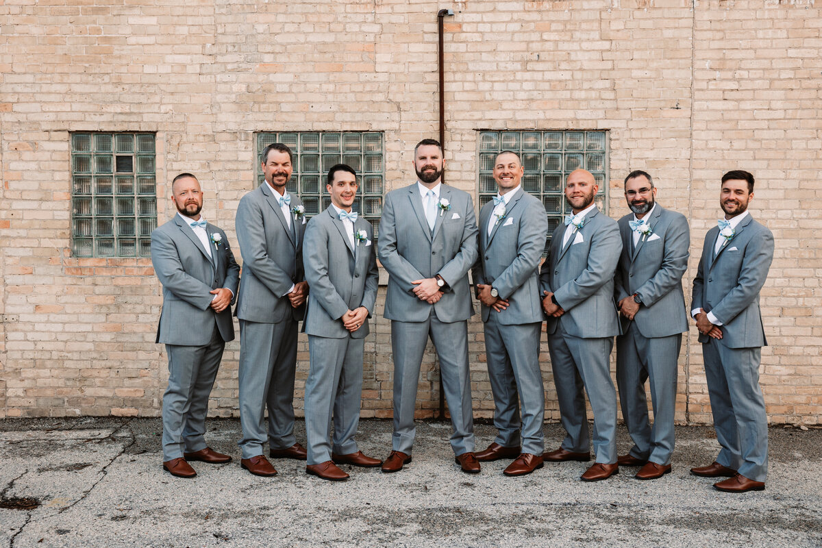 A groom stands with his groomsmen all with hands in front of them in matching grey suits