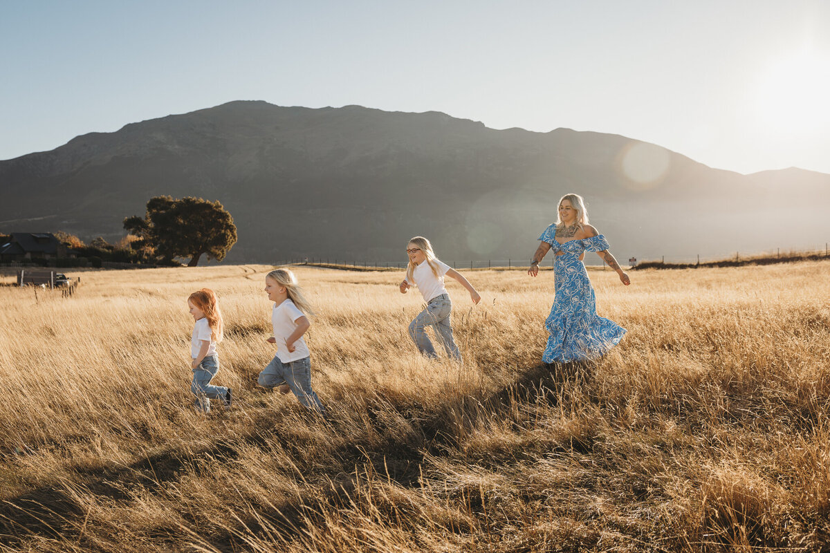 a mum and three daughters walking in a field while getting their pictures taken in Wanaka