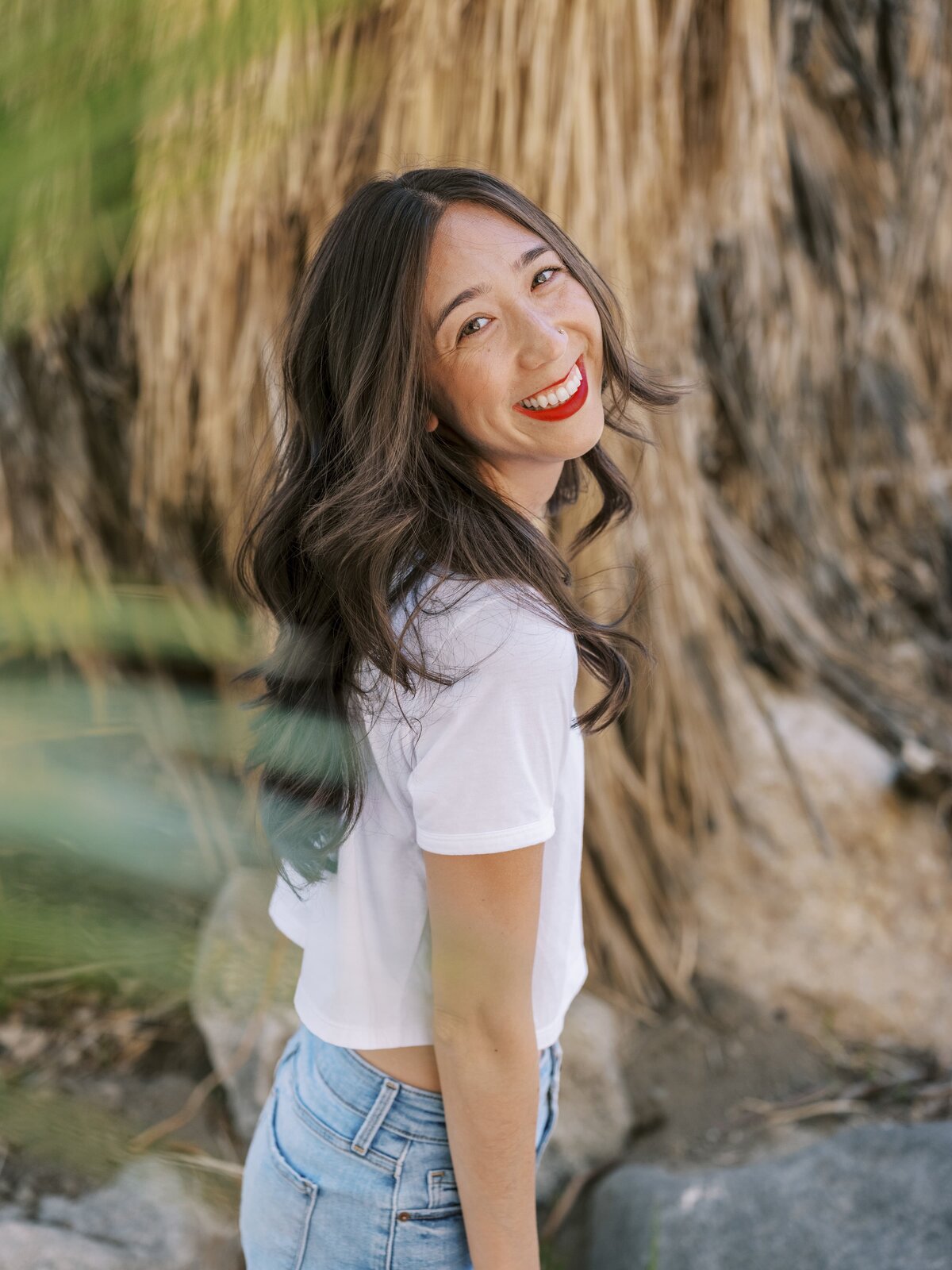Woman standing in a desert looking at the camera and smiling, wearing red lipstick
