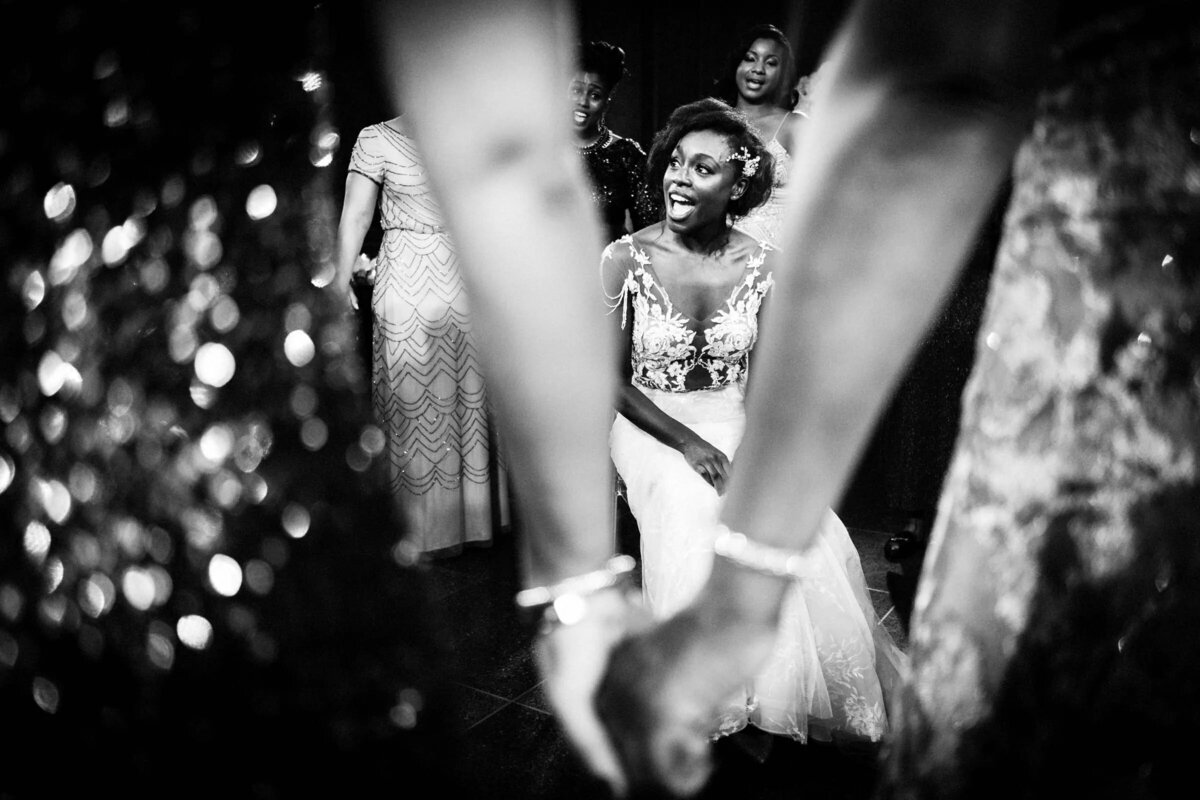 A bride sitting in a chair taken through two guests arms.