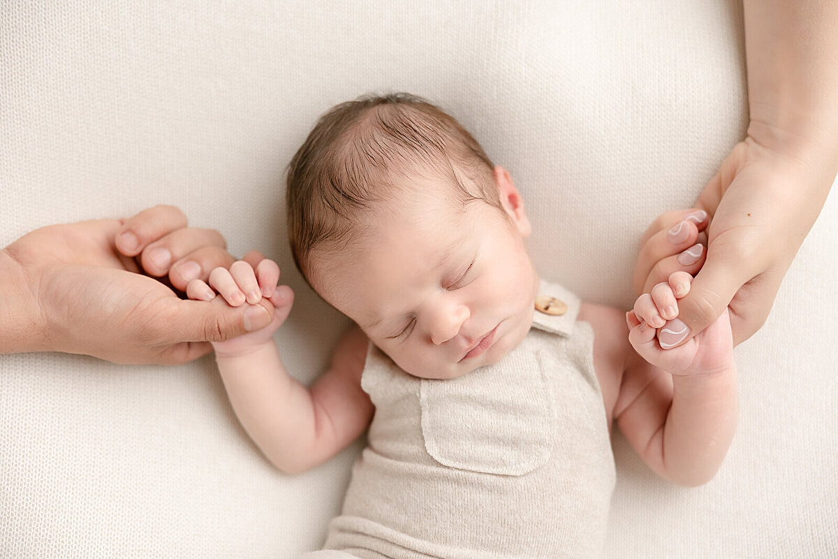 baby boy holding parents hands and sleeping in portland baby photography studio for his baby pictures