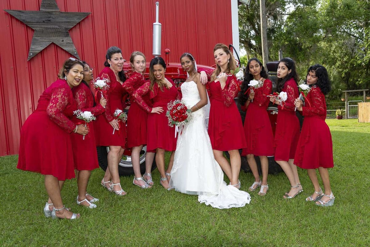 The bride and bridesmaids pose in front of a red barn.