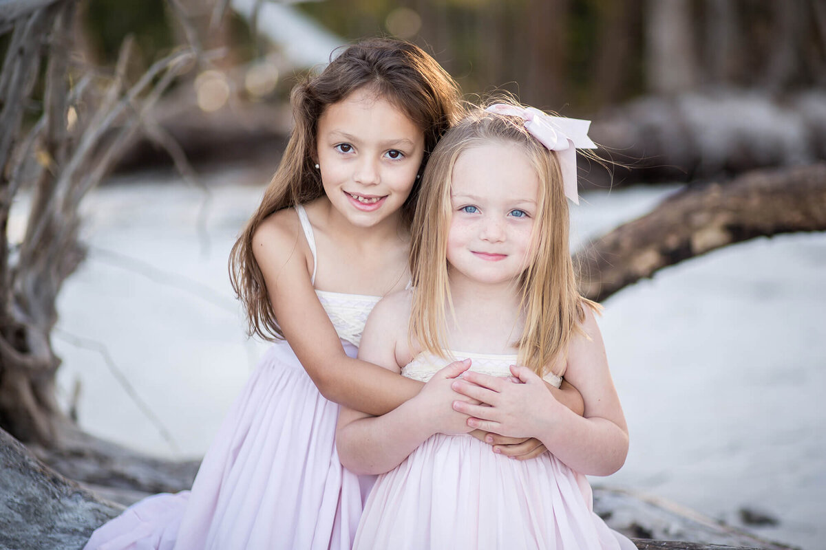 Older sister with her arms wrapped around younger sister dressed in pink 