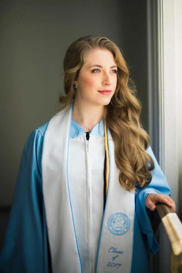 A girl looking out a window with a graduation gown on.