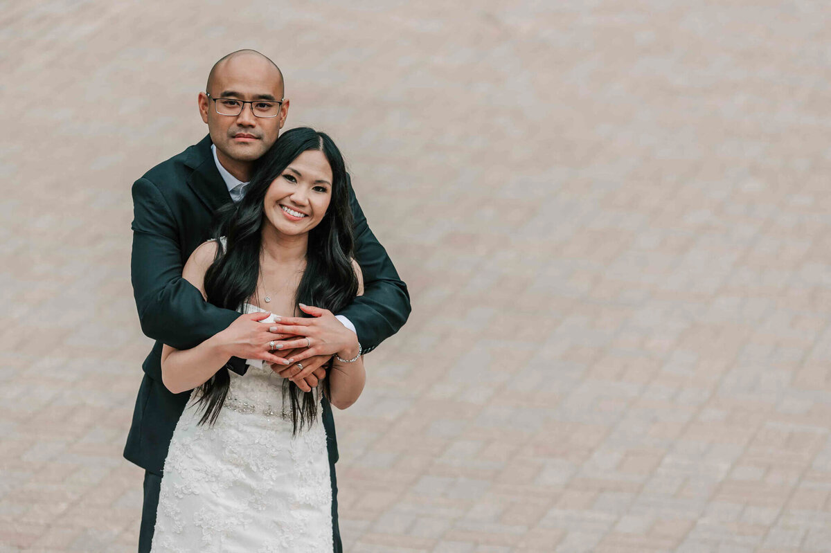 Groom standing behind bride with his arms wrapped around her.
