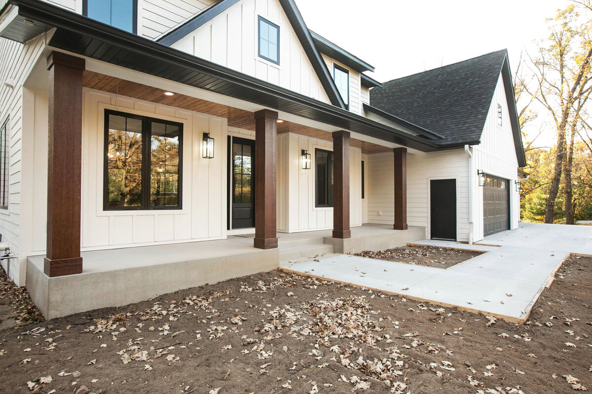 Exterior view of custom home in Big Lake Township, Minnesota with farmhouse details, cream siding, wood pillars and front porch built by Cornerstone Custom Builds