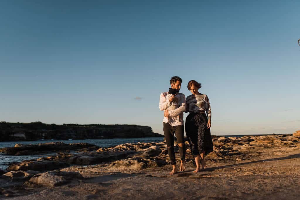 Parents carrying their young baby at sunset on a Sydney beach – joyful lifestyle family photography.