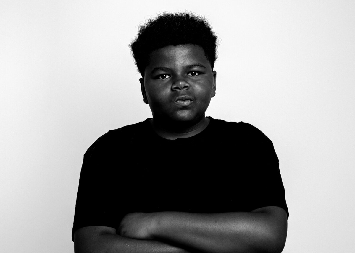 Confident black and white studio portrait of Shabaz Robinson smirking in a solid black shirt. Holly Springs NC end-of-year photoshoot 2025.