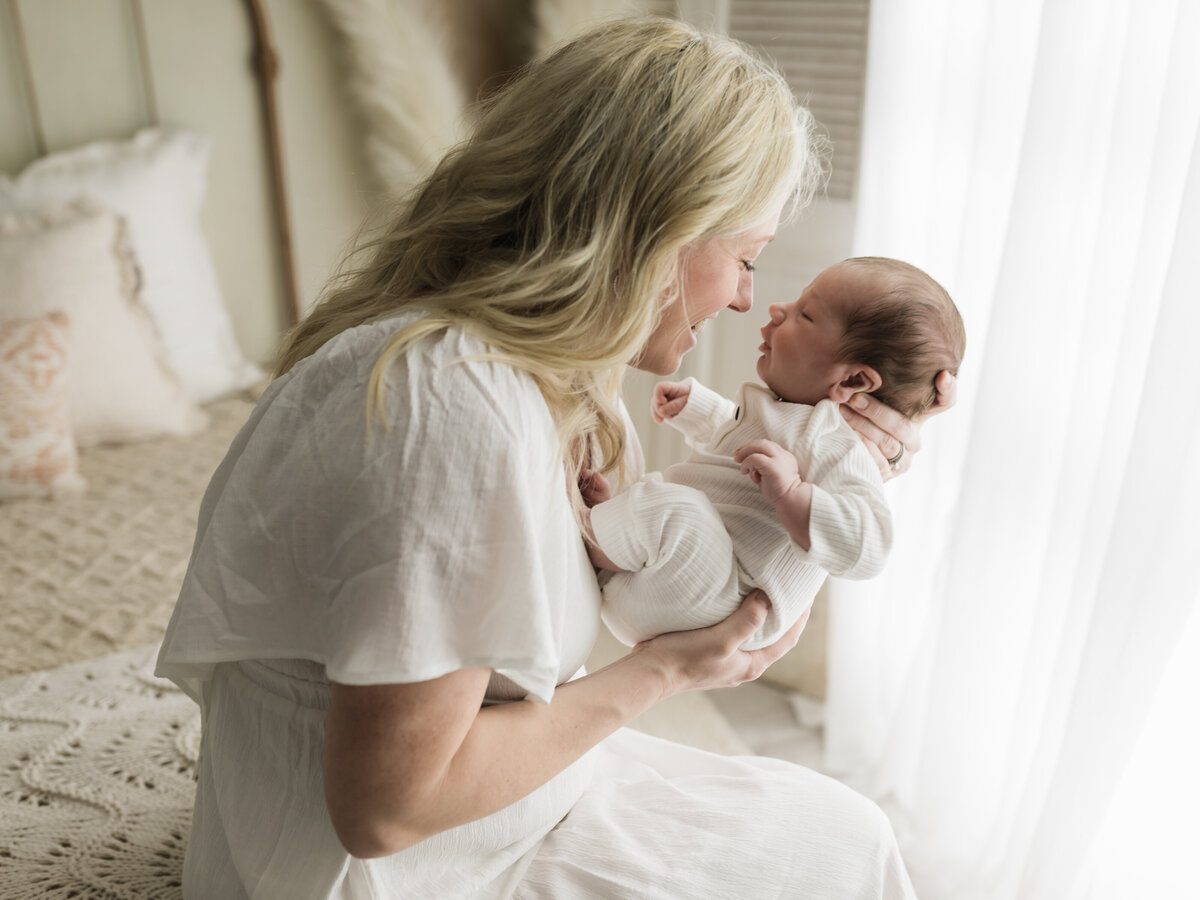 mom holding newborn baby boy in white onesie for studio photoshoot cleveland newborn photographer