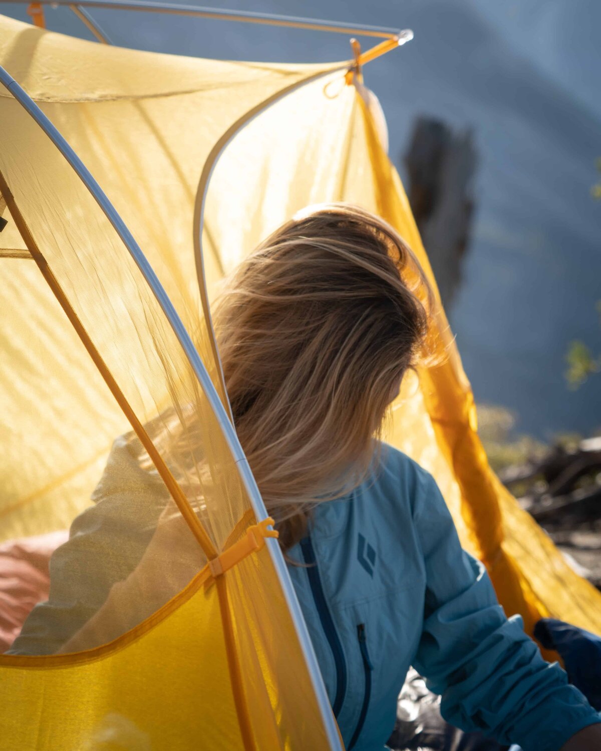 Woman in blue Backcountry jacket coming out of a yellow tent