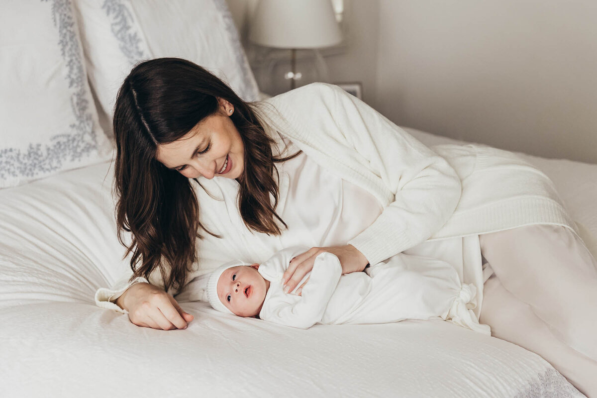 a mother lays on her bed with her sweet newborn baby in their Carlsbad home